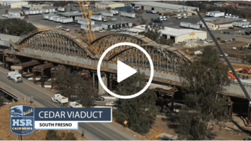 Thumbnail of Fall 2021 Construction Update Video, showing superimposed play button to induce click, showing the in-progress signature Cedar Viaduct arches over State Route 99, in the southern part of the City of Fresno.