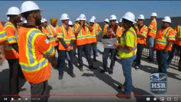 People wearing hard hats and safety vests standing and listening to a presenter