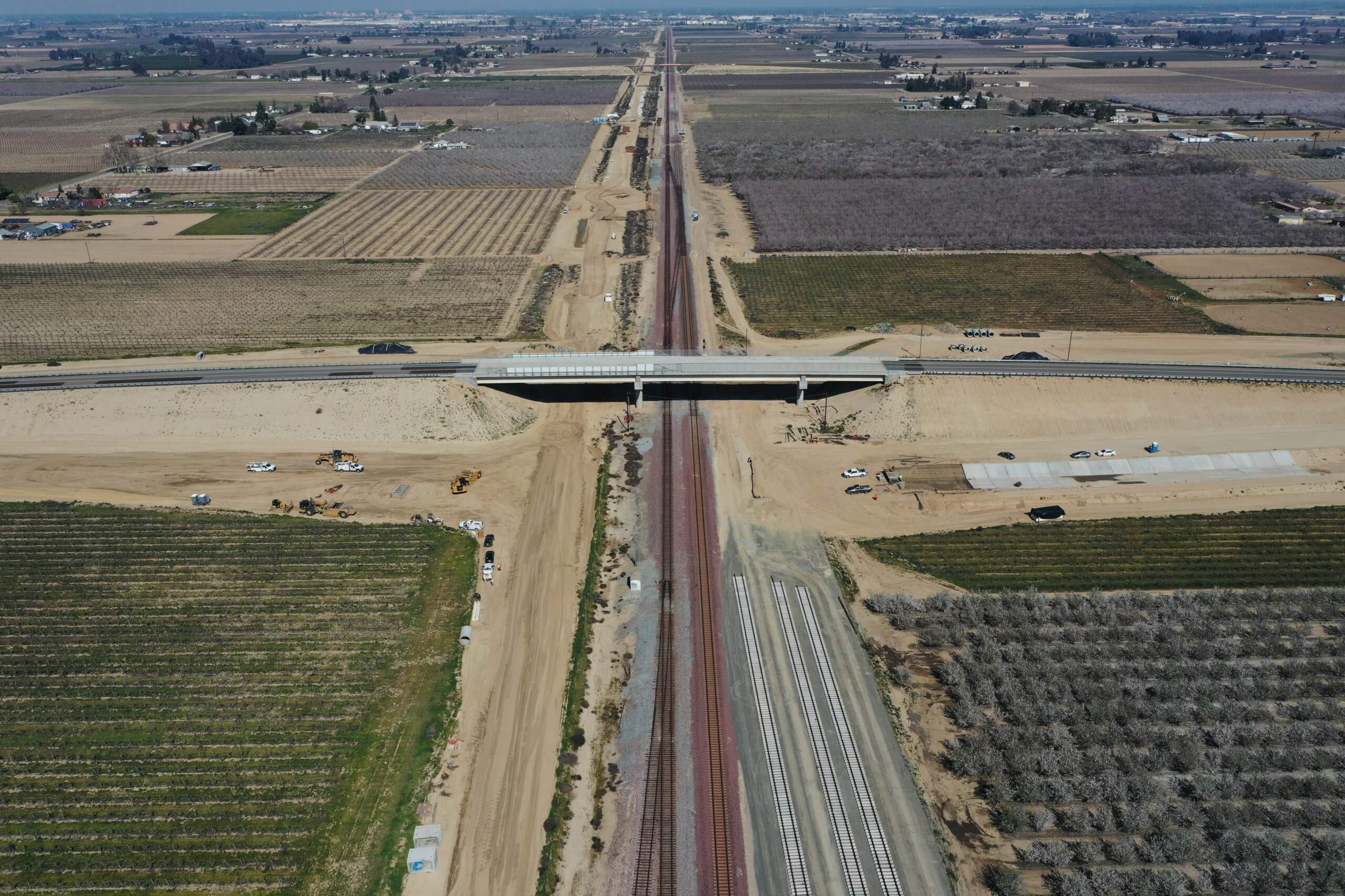 An image of the South Avenue Grade Separation in the middle, which shows the structure from the air and orchards all around, with the freight railroad tracks below heading straigh off to the horizon, beside where HSR tracks will eventually be laid, with the road crossing on the structure, rising on earthen berms to either side.