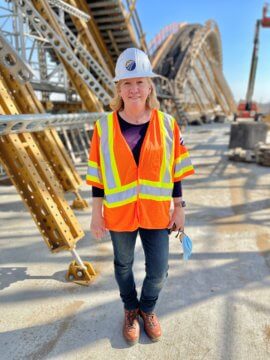 LaDonna DiCamillio in hardhat and safety vest standing on top of arches structure under construction 