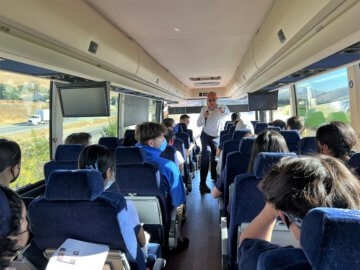 Man speaking in front of a group of students on a bus ride. 