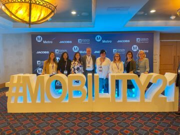 Group of 8 people standing in front of a very large sign that reads Mobility 21. 