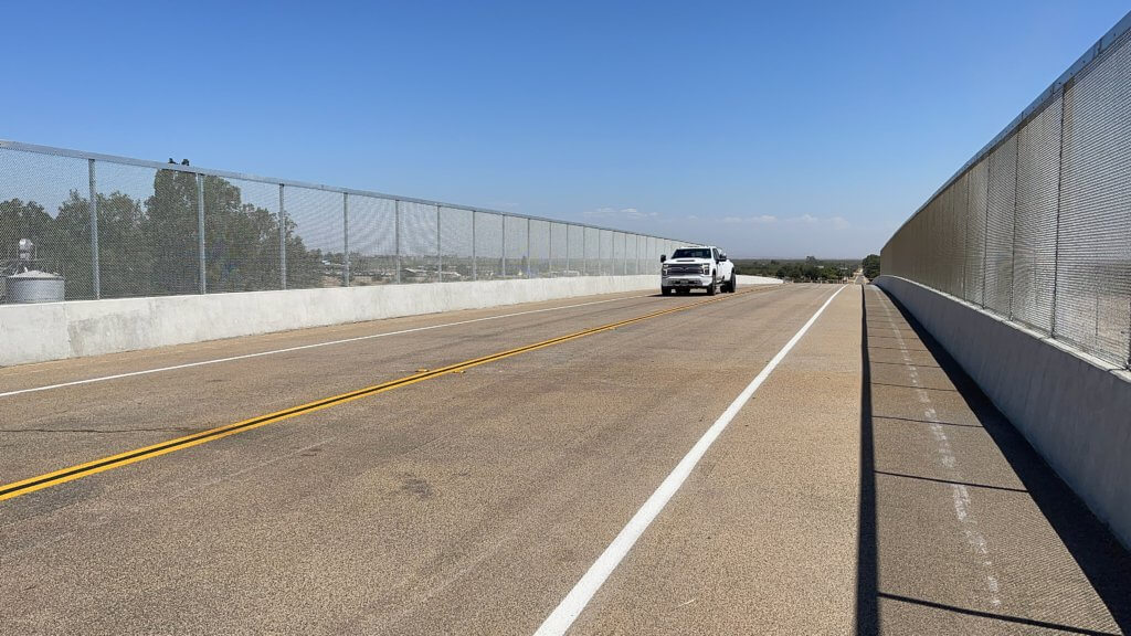 A pickup truck drives on the newly compelted and opened Avenue 15 1/2 grade separation. Fresh painted lane lines are visible, and a guardrail.