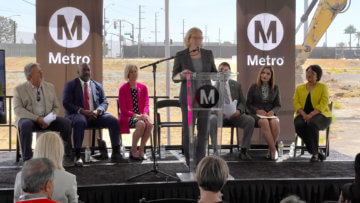 woman at podium speaking on stage with men and women seated behind her and Metro banners in background