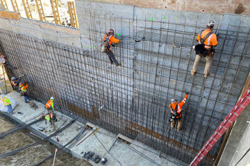 workers climbing on rebar structure along concrete wall