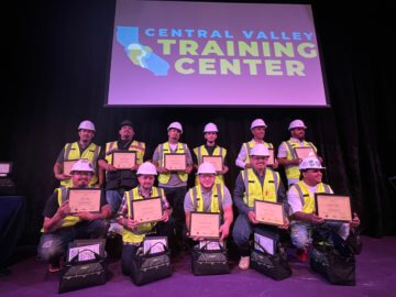 Most recent CVTC cohort line up for a photo commemorating their graduation, with their certificates and tool bags in front of a banner which reads 