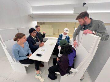 Five people testing a seating option in a rail car mock up space. One person standing explaining the seating. 