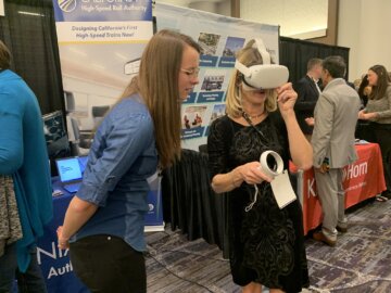 Woman wearing a VR headset and holding a controller with another woman looking over her shoulder, guiding her.