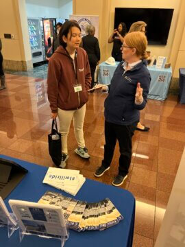 Woman explaining something to a student in front of outreach table. 
