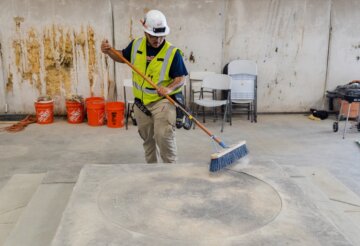 Adrian Vasquez, wearing safety gear, brushes off a cement slab with a broom
