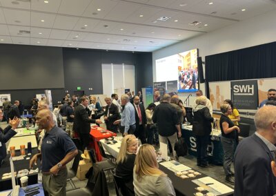 Scores of small business representatives mill about in a large auditorium during the fair, with dozens of prospective employers sitting and standing at their tables with informational items and displays.