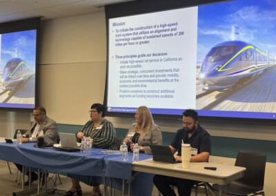 High-speed rail representatives sit for a panel presentation on the project with a projected image of the project behind them.