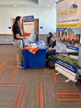 Two students talking with representatives from the California High-Speed Rail Authority at an outreach event. 