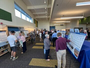 Attendees gather around informational boards at an open house. 