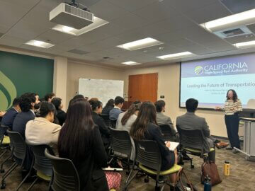 Department leader provides a presentation in front of a group of 20 or so young professionals. The presentation title reads, Leading the Future of Transportation. 