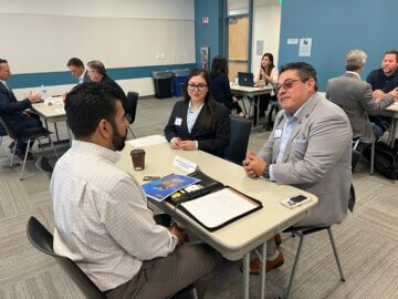 Three people at a table chat about possible partnership and contracting opportunities at one-on-one small group discussions. 