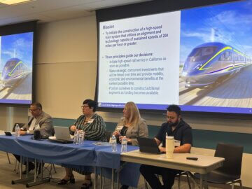 Four people on stage in a panel talking about a project. 