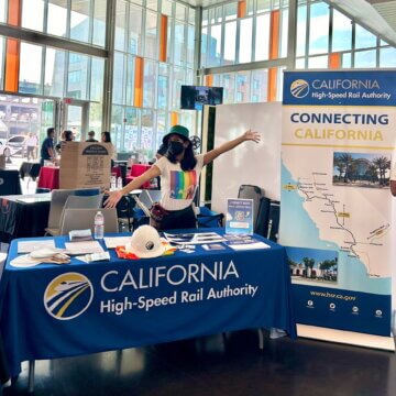 High-speed rail staff member smiles and welcomes students to an outreach booth. 