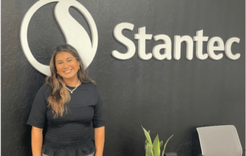 Intern Alondra Martinez smiles while standing in front of company sign that reads Stantec. 