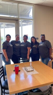 Five women smile and are wearing matching grey t-shirts. 