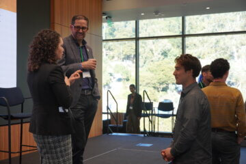 Two people that were on a panel talking and laughing with a student after the event.