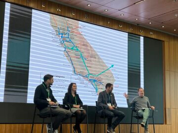 Four panelists on a stage during a panel presentation with a map of California in the background. 