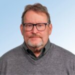 Headshot of Kevin Gilson. He's wearing a gray sweater, gray button up shirt, and glasses.