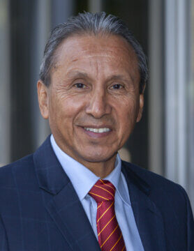 Portrait of Authority Board Member Henry Perea dressed in a blue suit, light blue shirt, and patterned red tie.
